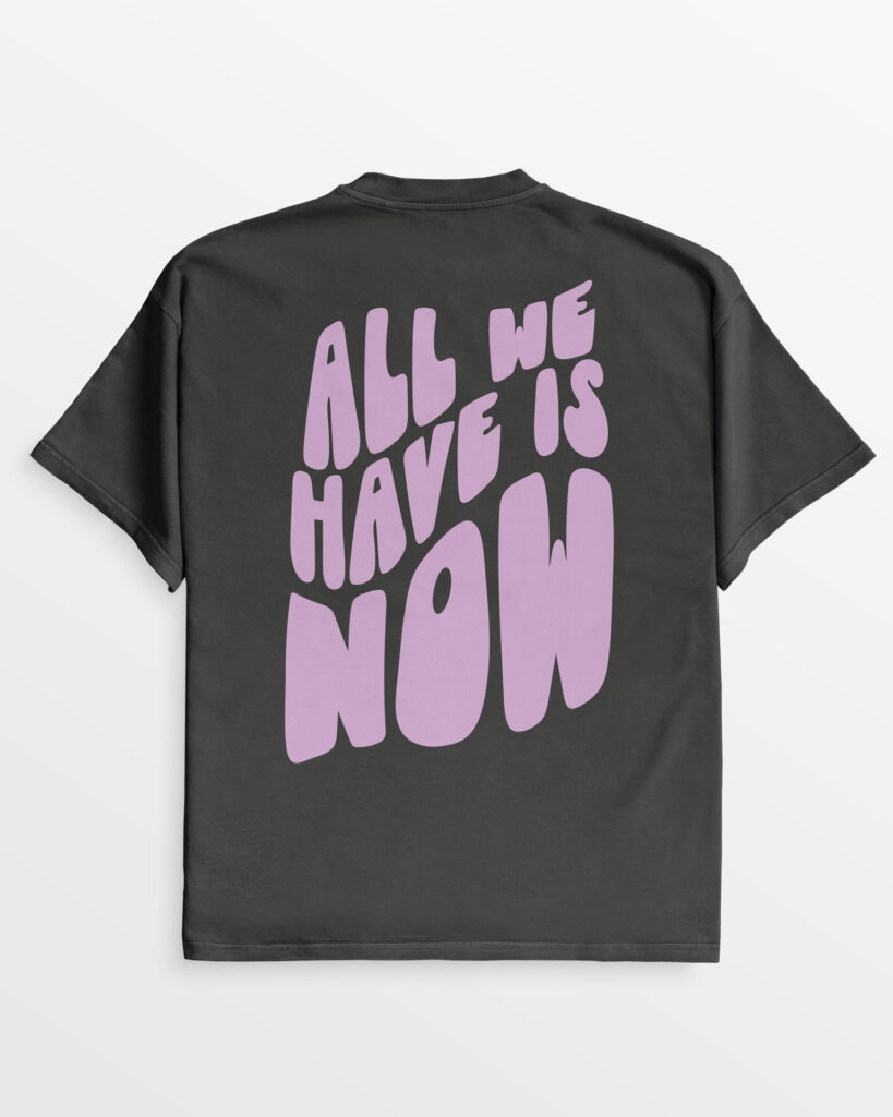 Rückseite des oversize 'All we have is now' T-Shirts in Vintage-Schwarz mit großer lila Schrift, aus 100% Bio-Baumwolle