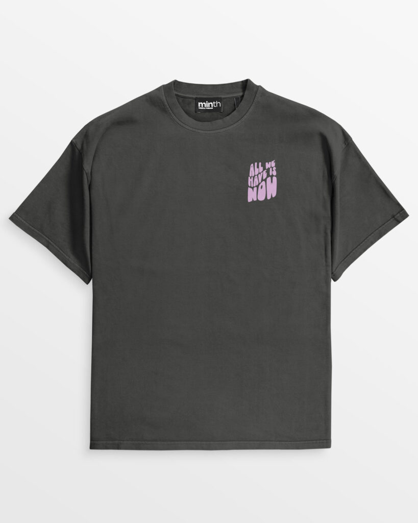 Vorderseite des oversize 'All we have is now' T-Shirts in Vintage-Schwarz mit lila Schrift auf der Brust, aus 100% Bio-Baumwolle.